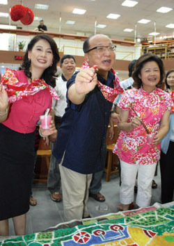身披客家花布領巾的台中市長胡志強（中），與區長葉玉錦（右）、文化局長葉樹珊（左），於東勢區圖書館重新啟用時，於兒童繪畫中著色。